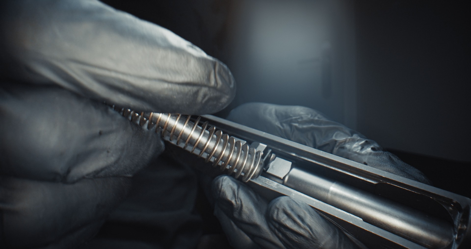 Gun reassembly after cleaning and maintenance. Man in protective gloves re-inserting the barrel and the recoil spring into the case. Proper firearm care